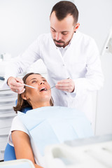 Dentist is treating woman patient which is sitting chair in clinic