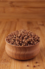 Buckwheat brown in wooden bowl on brown bamboo board, closeup. Healthy dietary groats  background.