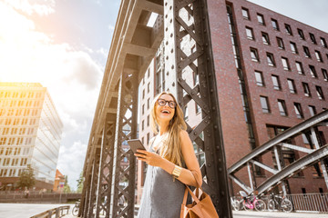 Lifestyle portrait of a stylish business woman sitting with phone outdoors on the iron bridge...