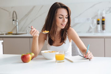 Obraz na płótnie Canvas Smiling attractive woman eating corn flakes cereal for breakfast