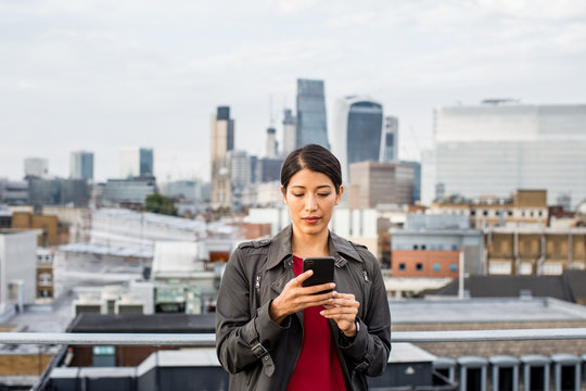 Businesswoman using smartphone with London city skyline