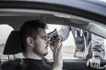 A thief, a criminal with a pistol threat, is trying to steal a car, holding a pointed gun in a car...