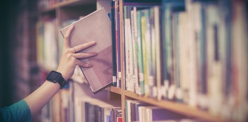 Students hand with smartwatch picking book from bookshelf