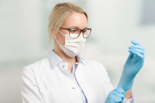 Junge hübsche Ärztin mit Mundschutz zieht Handschuhe an