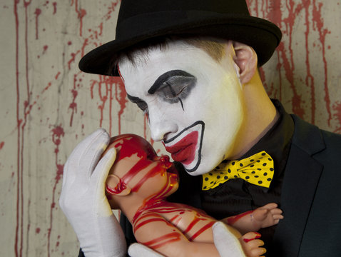 evil clown playing with bloody doll