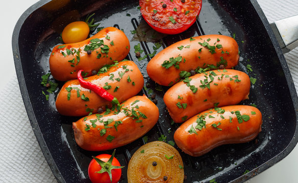 Fried sausages with herbs and vegetables in grill pan at white background