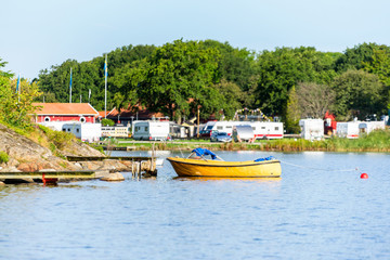 Fototapeta na wymiar One open yellow motorboat moored to a pier with camping site in background. Location Karlskrona, Sweden.