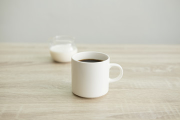 Fototapeta na wymiar WHITE COFFEE CUP WITH MILK JAR White coffee cup with transparent milk jar on the wood table. 