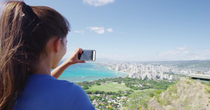 Female hiker photographing Waikiki Beach and Honolulu through smartphone. Young woman is enjoying view from Diamond Head State Monument during summer vacation. RED EPIC SLOW MOTION.