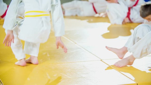 Kids are doing different exercises when they are warming up before judo practise. They are wearing white uniforms.