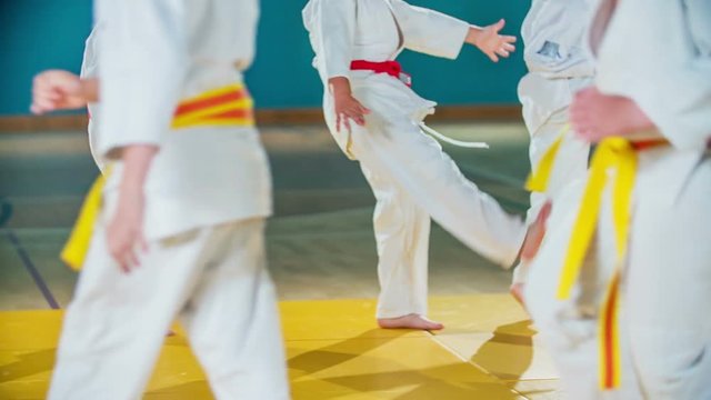 Kids are warming up before judo practise. They are wearing white uniforms and belts of different colours.