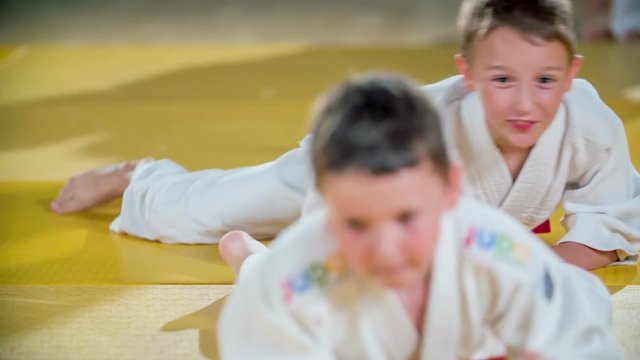Children are enjoying a warm up before judo practise. They are crawling on the mattresses and are wearing white judo uniforms.
