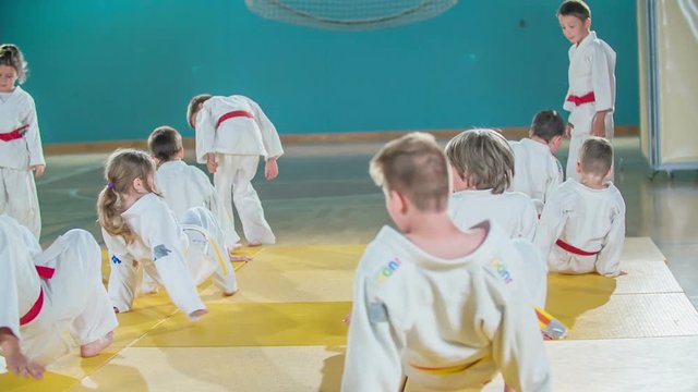 Children are walking backwards when they are warming up in judo practise. They are wearing white judo uniforms.