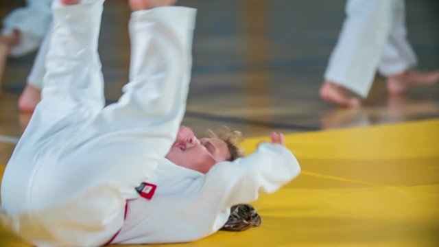 A small girl is doing a somersault on a mat in the gym. Students are warming up before judo practise in a school gym.