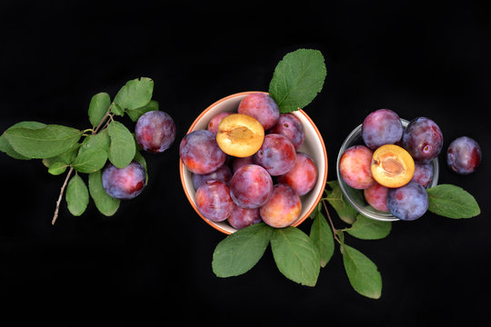 Plums in bowl on dark background, top view.