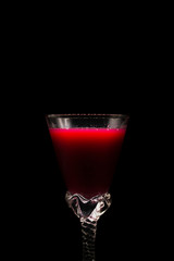 Red cocktail in a wine glass of black background.