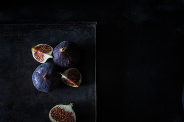 Feigen als ganze Frucht und im Anschnitt von oben auf schwarzem Untergrund bei Tageslicht fotografiert