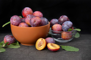 Ripe plums in bowl on dark background.