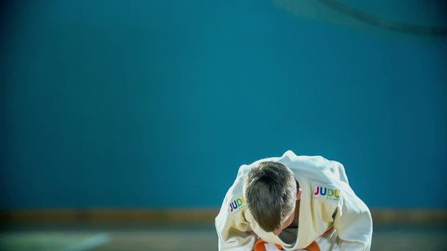 Two students are taking two bows and are shaking hands before judo practise. They are wearing white uniforms and orange belts.