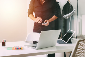 Fashion designer working with mobile phone and using laptop with digital tablet computer in modern studio