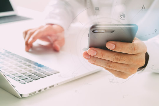 close up of businessman using mobile phone and laptop computer on white desk in modern office