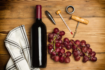 Botella de vino tinto con uvas moradas y accesorios para el vino sobre fondo de madera rústica. Vista superior