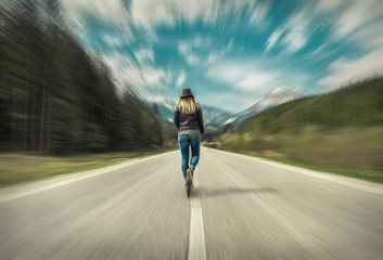 Fototapeta premium Woman on her kick scooter on the road around mountains, under s