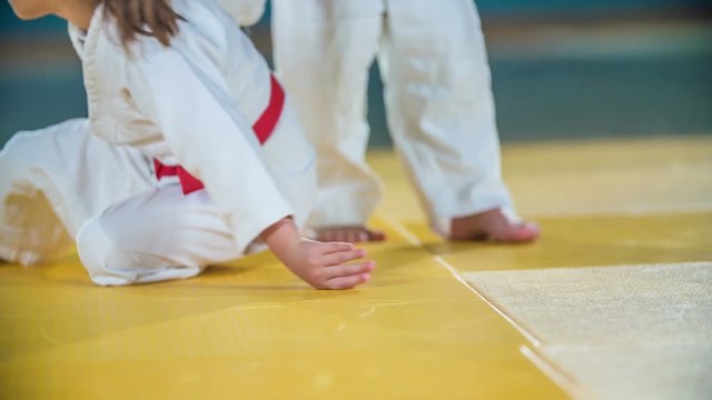 One girl is helpig the other girl getting back up on her feet. They were practising judo. They are wearing white uniforms and red belts.