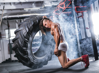 Fototapeta na wymiar Muscular athletic bodybuilder flipping tire in cross gym