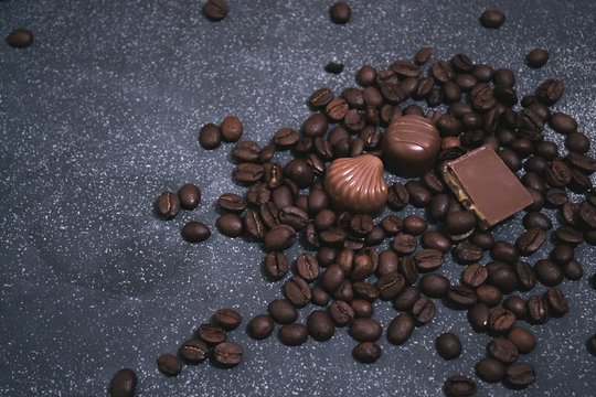 Coffee beans and tiles of dark chocolate on a dark matte background.