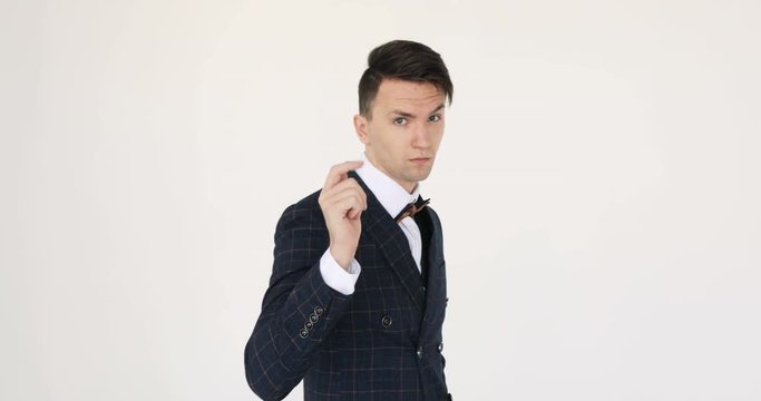 Attractive young businessman is looking at the camera. Closeup video of an attractive businessman in his 20s, wearing a blue suit and the bow tie. Against a white background.