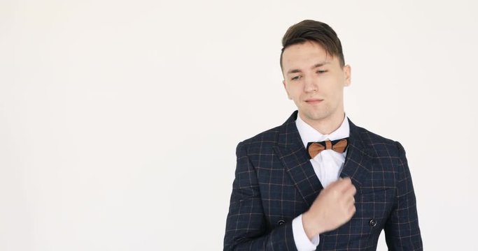 Attractive young businessman is looking at the camera. Closeup video of an attractive businessman in his 20s, wearing a blue suit and the bow tie. Against a white background.