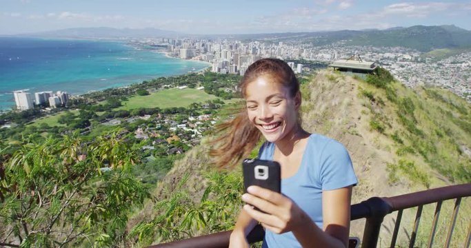 Happy hiker taking selfie through smartphone against Waikiki Beach and Honolulu. Woman is enjoying vacation at Diamond Head State Monument. She is photographing through mobile phone at Oahu.