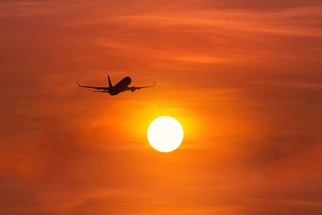   Silhouette passenger airplane flying away in to sky high altitude above the sun during sunset