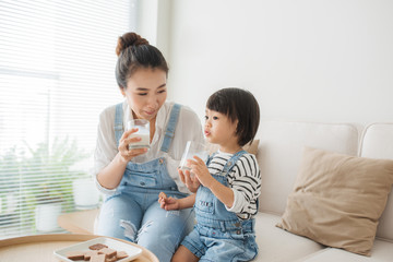 Adorable girl eating cookies and drinking milk with her mother.