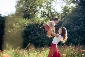Young beautiful happy mother with her little 2 year old son in field of poppies in the sun. Summer.