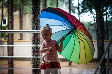 Cute blonde small girl smiling and holding colorful umbrella
