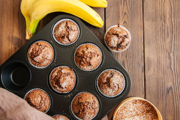 Homemade banana chocolate muffins sprinkled with sugar in a baking form on a wooden background. Top...