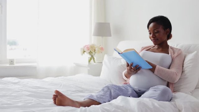 happy pregnant african woman reading book at home