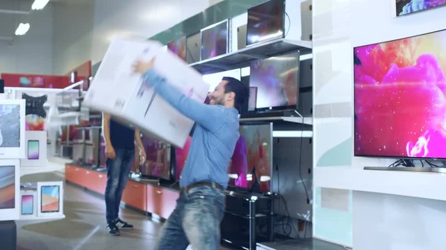 Young Man in Electronics Store Purchased Big Drone and Dances Happily with the Box. Bright and Modern Store Has all the Latest Devices in Store. Shot on RED EPIC-W 8K Helium Cinema Camera.