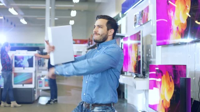 Young Man in Electronics Store Purchased Latest Model of the Tablet Computer and Dances Happily with the Box. Bright and Modern Store Has all the Latest Devices in Store. 4K UHD.