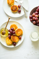 Breakfast with mini cheesecakes, grapes, cream and honey on a white plate