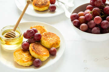 Breakfast with mini cheesecakes, grapes, cream and honey on a white plate