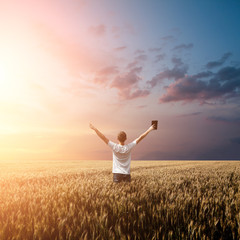 Man holding up Bible in a wheat field