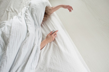 Morning, the woman under the blanket, turns off the alarm clock or watching the social network