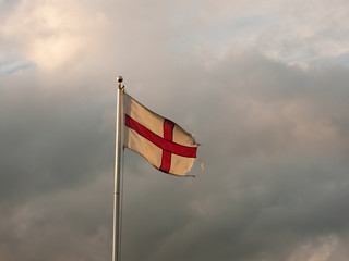 england flag flying with cloudy dramatic skies during sunset