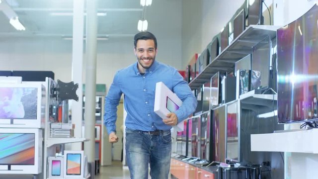 In the Electronics Store Young Man Holds Newly Purchased Computer Tablet  and Happily Jumps with it. Shot in Slow Motion. Store is Modern, Bright and Has All the Latest Devices. 