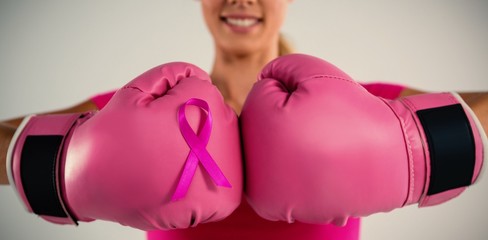 Mid section of smiling woman with boxing gloves and pink ribbon
