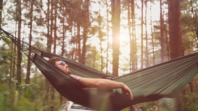 A young man relaxes on a hammock in the forest.