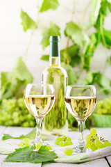 Glasses with white wine, fresh grapes and a bottle of white wine on a wooden table.